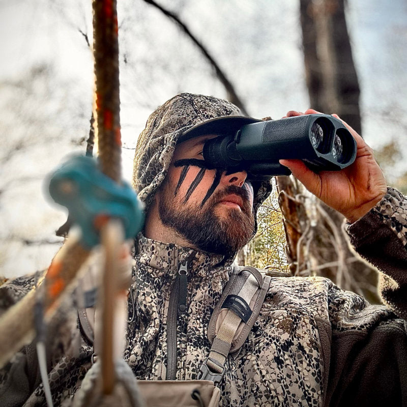 Man outdoors, wearing camo, looking through Alpen Apex Steady HD Binoculars